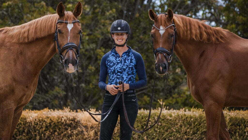 A person wearing a helmet and blue patterned shirt stands outdoors holding the reins of two brown horses, one on each side, with trees and bushes in the background—like a perfect image for a Sales Page Template.