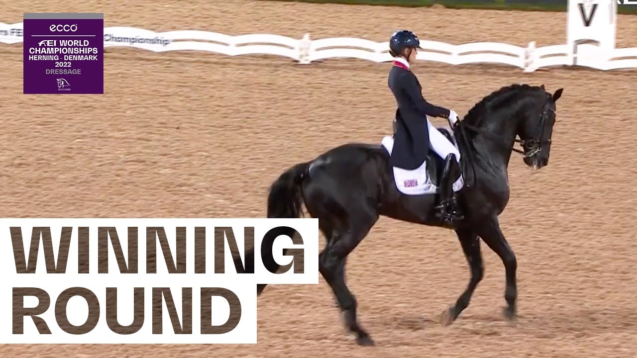 A dressage rider in a dark jacket and helmet guides a black horse in an arena. Text reads WINNING ROUND. The top left corner shows FEI World Championships Herning - Denmark 2022 Dressage logo.
