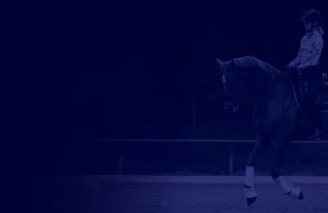 A person wearing a helmet rides a horse in an outdoor arena, both horse and rider are facing right. The image’s dark blue overlay adds drama, evoking the focus and intensity of a Scale Masterclass training session.