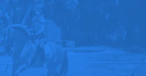 A person wearing a helmet rides a horse outdoors during the 30 Days to Round 2023 event. The image has a blue overlay, with trees and a fence visible in the background.