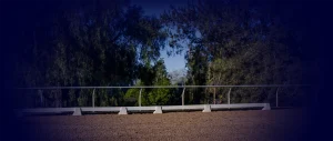 A sandy arena bordered by a white rail fence hosts the Groundwork Masterclass, set against lush green trees and a clear blue sky, with a dark blue gradient in the top corners of the image.
