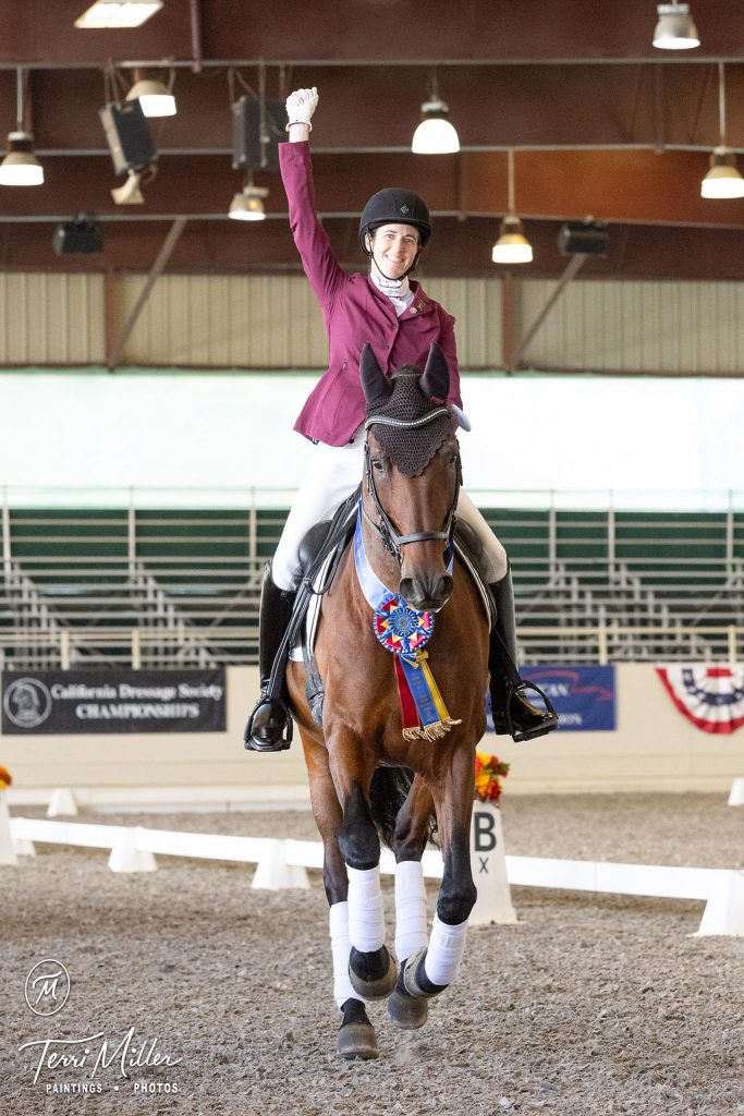 Dressage rider celebrating a win, horse is wearing a winner's sash.