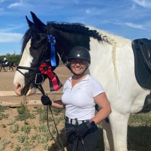 Carole Online student Carole posing with her horse with a first and second place rosettes pinned to her horse.