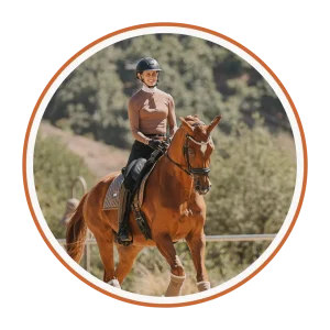 A person wearing a helmet and brown riding attire rides a chestnut horse outdoors, surrounded by greenery—capturing the essence of contact and connection with nature.