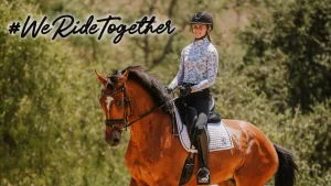 A person in riding gear smiles while riding a brown horse outdoors at Thunderbird Show Park. The background is green and leafy, with “#WeRideTogether” written in bold script in the top left corner, highlighting this exciting event.