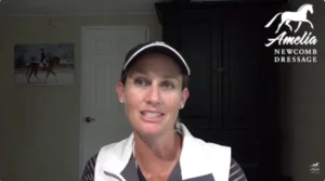 A woman wearing a white vest and cap speaks indoors. Behind her is a dark cabinet, a white door, and a painting of a horse and rider. The top right shows the Amelia Newcomb Dressage logo, reflecting her passion for Dressage lessons.