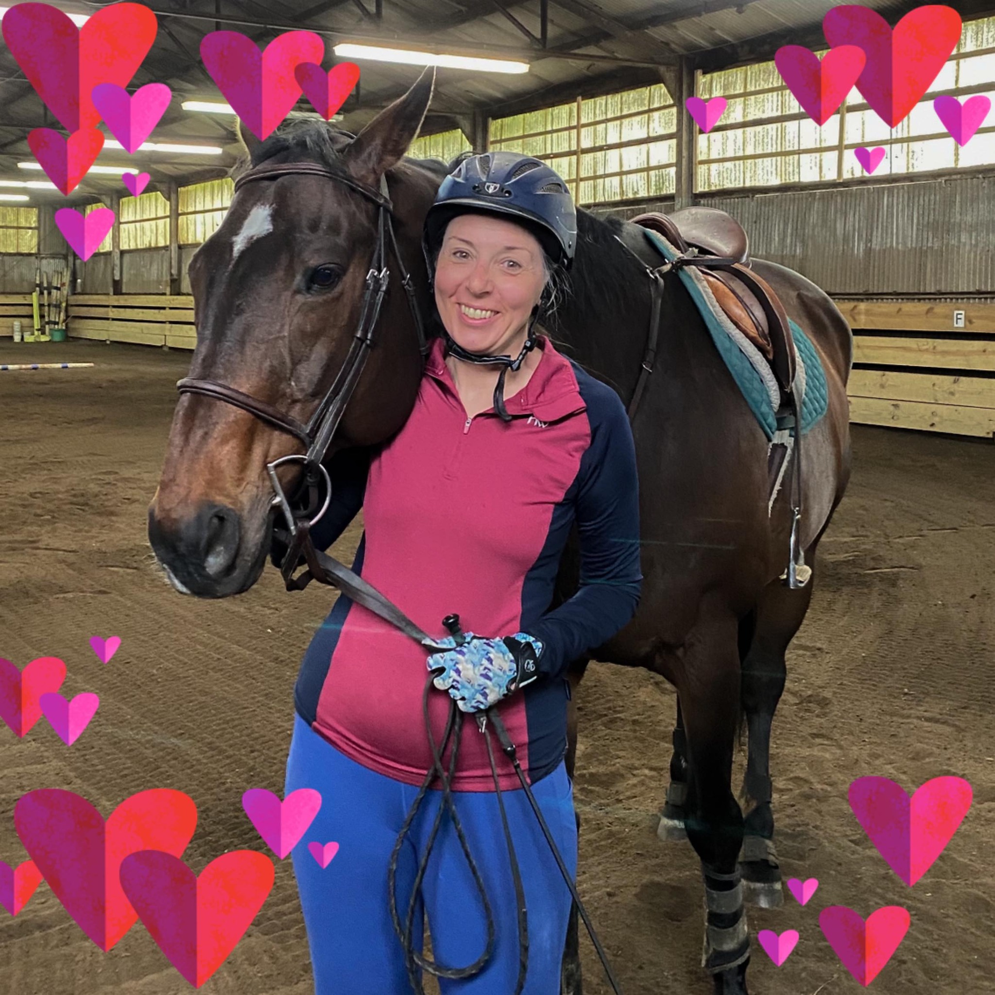 A smiling student in casual riding attire stands alongside Brandy, a dark bay horse, within an indoor arena. The image is adorned with pink and red heart graphics, lending a warm and supportive ambiance.