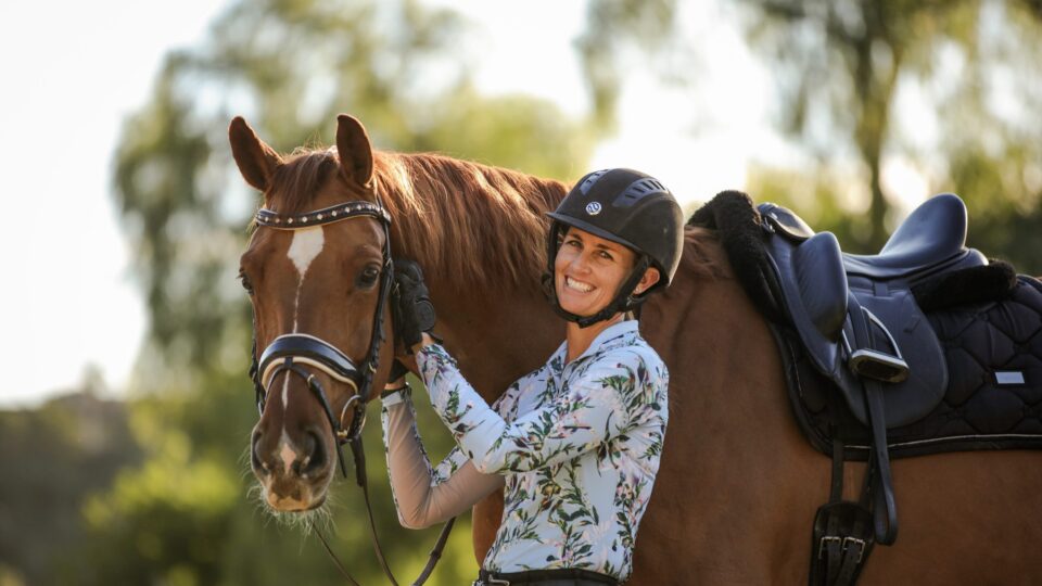 Amelia Newcomb smiling and posing with her chestnut horse who is wearing a dressage saddle and snaffle bridle.