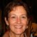 A middle-aged woman with short brown hair, wearing earrings and a brown jacket, smiles warmly at the camera. Set against a dark, blurred background, her confident expression could grace a 2024 Sale Page or Training Scale guide.
