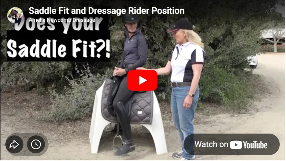Two women are outdoors; one sits on a saddle positioned on a white stand while the other points beside her. Text asks: Does your Saddle Fit?! Perfect for learning about saddle fit and dressage rider position. Video title: Saddle Fit and Dressage Rider Position.