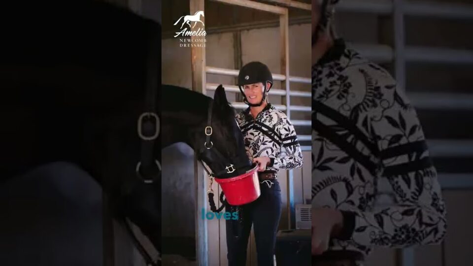 A smiling person in a helmet and patterned shirt holds a red feed bucket for a black horse inside a stable. The horses head is lowered into the bucket. Text and a logo are visible on the image.