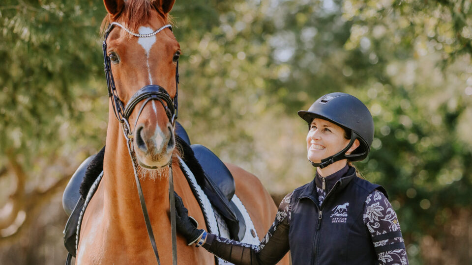 A smiling person in equestrian gear and helmet stands beside a brown horse with bridle and saddle, outdoors among green trees—perfect for the November 2023 newsletter cover.